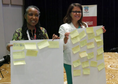 Two women stand side by side holding flip chart paper with post-it notes on them.